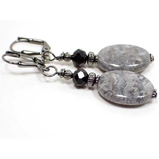Photo of the handmade gemstone earrings. The metal is gunmetal gray in color. There are faceted black glass crystal beads at the top. The bottom beads are crazy lace agate gemstone and are puffy oval shaped with marbled shades of mostly gray and white.