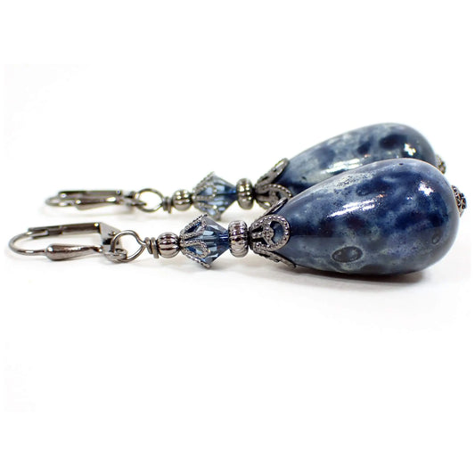 Side view of the large handmade teardrop earrings. The metal is gunmetal gray in color. There are faceted blue glass crystal beads at the top. The bottom beads are large acrylic teardrops with a marbled denim blue pattern.