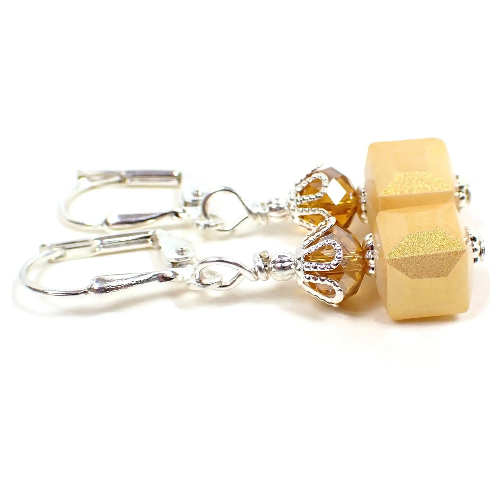 Side view of the handmade small cube earrings. The metal is silver plated in color. There are faceted glass beads at the top in a golden citrine orange color. The bottom square cube beads are a light orange with a golden sheen on the outside.