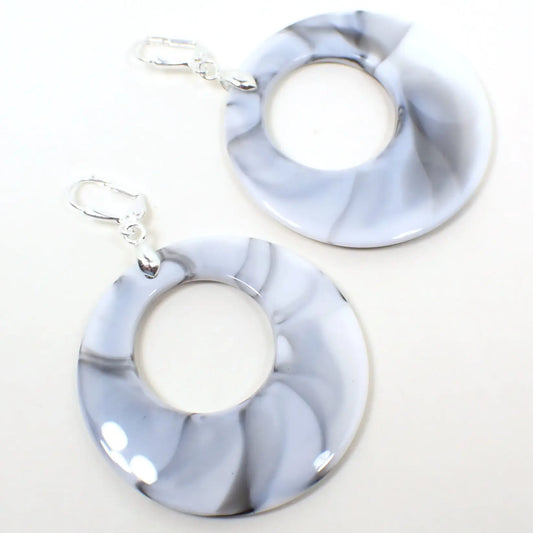 Enlarged top view of the handmade acrylic hoop earrings. The metal is silver tone in color. They have large round acrylic hoop drops that are white with gray and black marbled in here and there.