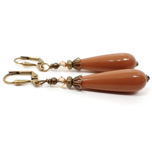 Side view of the handmade teardrop earrings made with vintage lucite beads. The metal is antiqued brass in color. There are faceted glass beads in light brown at the top. The bottom lucite beads are a terracotta brown in color.