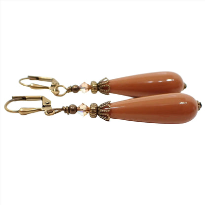Side view of the handmade teardrop earrings made with vintage lucite beads. The metal is antiqued brass in color. There are faceted glass beads in light brown at the top. The bottom lucite beads are a terracotta brown in color.
