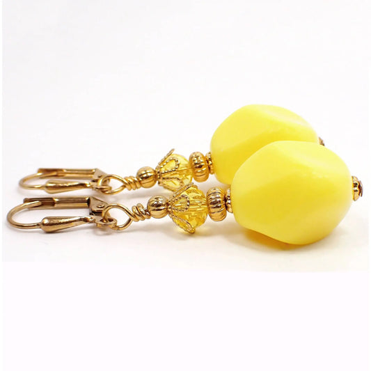 Side view of the handmade chunky nugget style drop earrings. The metal is gold plated in color. There are faceted glass crystal beads at the top in yellow. The bottom beads are vintage lucite and are irregularly shaped with faceted edges for a nugget style appearance. They are a bright yellow in color.