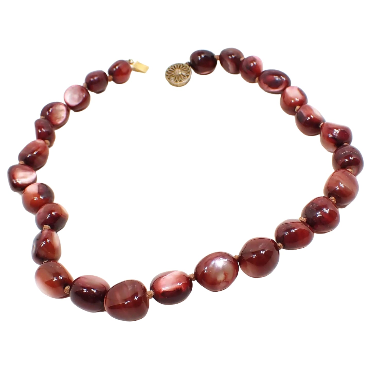 Front view of the Mid Century vintage shell beaded necklace. It is beaded with chunky nugget style dyed mother of pearl beads that have red and brown tones. The beads are hand knotted in between each one. There is a filigree vermeil gold over sterling box clasp at the end.