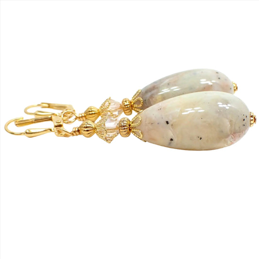 Side view of the handmade faux stone earrings. The metal is gold plated in color. There are faceted glass crystal beads on the top in a very light champagne color. The bottom lucite teardrop beads have marbled muted colors of tan, off white, white, orange, pink, and gray for an imitation stone appearance.