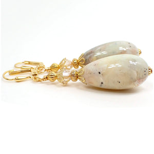 Side view of the handmade faux stone earrings. The metal is gold plated in color. There are faceted glass crystal beads on the top in a very light champagne color. The bottom lucite teardrop beads have marbled muted colors of tan, off white, white, orange, pink, and gray for an imitation stone appearance.