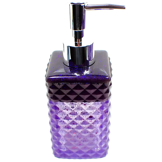 Side view of the handmade resin and glitter soap dispenser. It has a silver tone metallic plastic pump style top. It has a diamond pattern faceted design and a square shape. There is dark pearly purple resin at the top with tiny flecks of blue glitter. The rest of the dispenser is pearly semi translucent purple with chunky iridescent glitter.