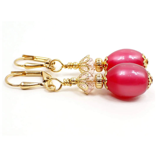 Side view of the handmade oval drop earrings with vintage lucite beads. The metal is gold plated in color. There is a new light pink faceted glass crystal bead at the top. The bottom moonglow lucite beads are oval shaped and are raspberry pink in color. Moonglow lucite has an inner glowy type effect as you move around in the light.