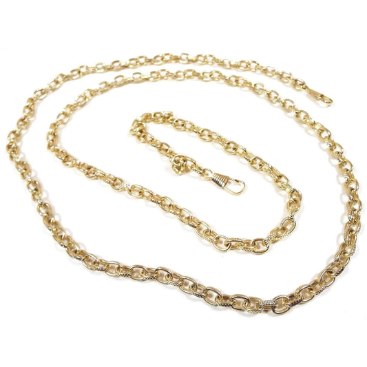 Angled view of the retro vintage fob or vest chain. The metal is gold tone plated in color. There are oval stamped textured cable chain links. The chain has snap clip ends.
