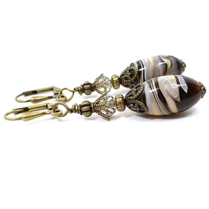 Side view of the handmade earrings with vintage lucite marbled beads. The metal is antiqued brass in color and there are faceted glass crystal beads at the tops. The bottoms have oval shaped lucite beads with swirls of brown, off white, black, and white.