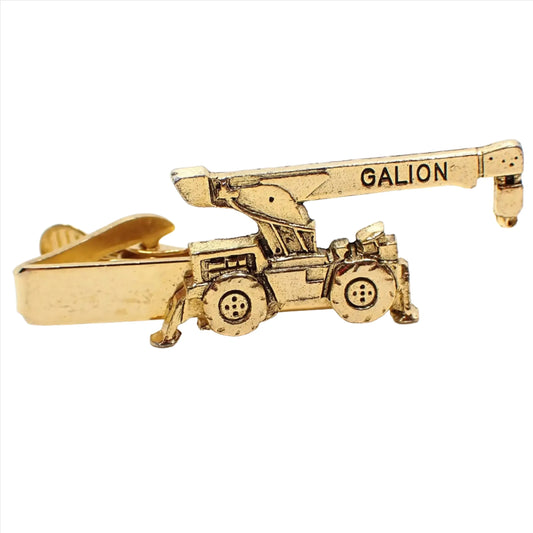 Front view of the Mid Century vintage Mercury Industries tie clip. It has a shape of a crane on the end with "Galion" on the top. The metal is gold tone plated in color.