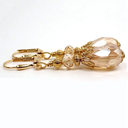 Side view of the vintage style light peach champagne color teardrop earrings. The metal is gold plated in color. There is a faceted glass crystal bead at the top and a faceted glass crystal teardrop bead at the bottom.