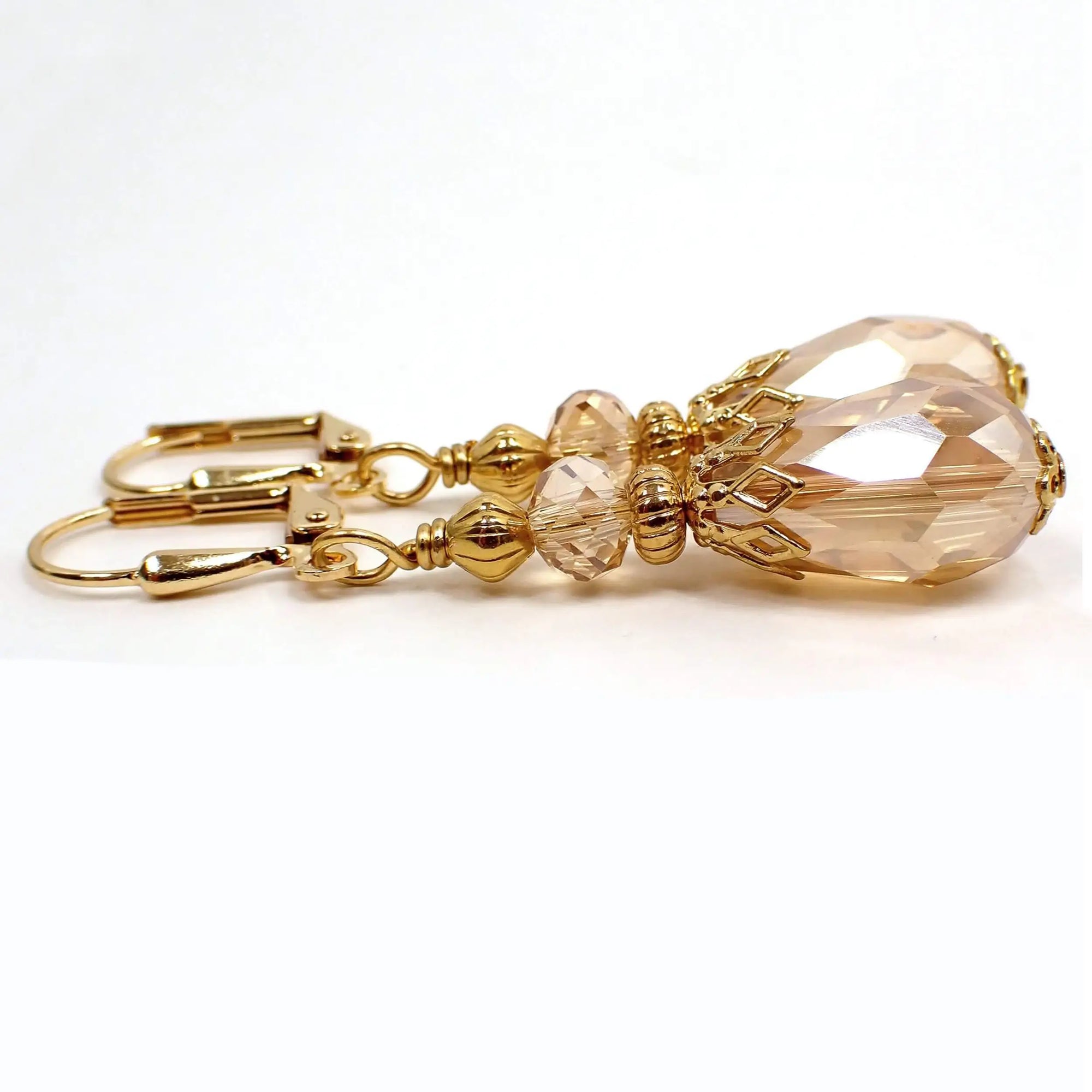 Side view of the vintage style light peach champagne color teardrop earrings. The metal is gold plated in color. There is a faceted glass crystal bead at the top and a faceted glass crystal teardrop bead at the bottom.