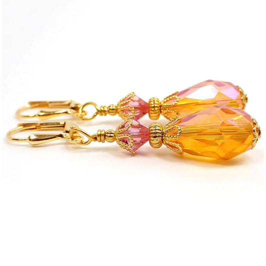 Side view of the handmade glass crystal teardrop earrings. The metal is gold tone in color. There is a faceted pink glass crystal bead at the top and a pink and orange combo faceted glass crystal teardrop bead at the bottom.