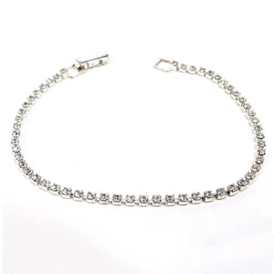 Angled view of the retro vintage thin rhinestone bracelet. The metal is silver tone in color. There is a single strand of prong set cup chain with small round clear rhinestones all the way down the bracelet. There is a snap lock clasp at the end.