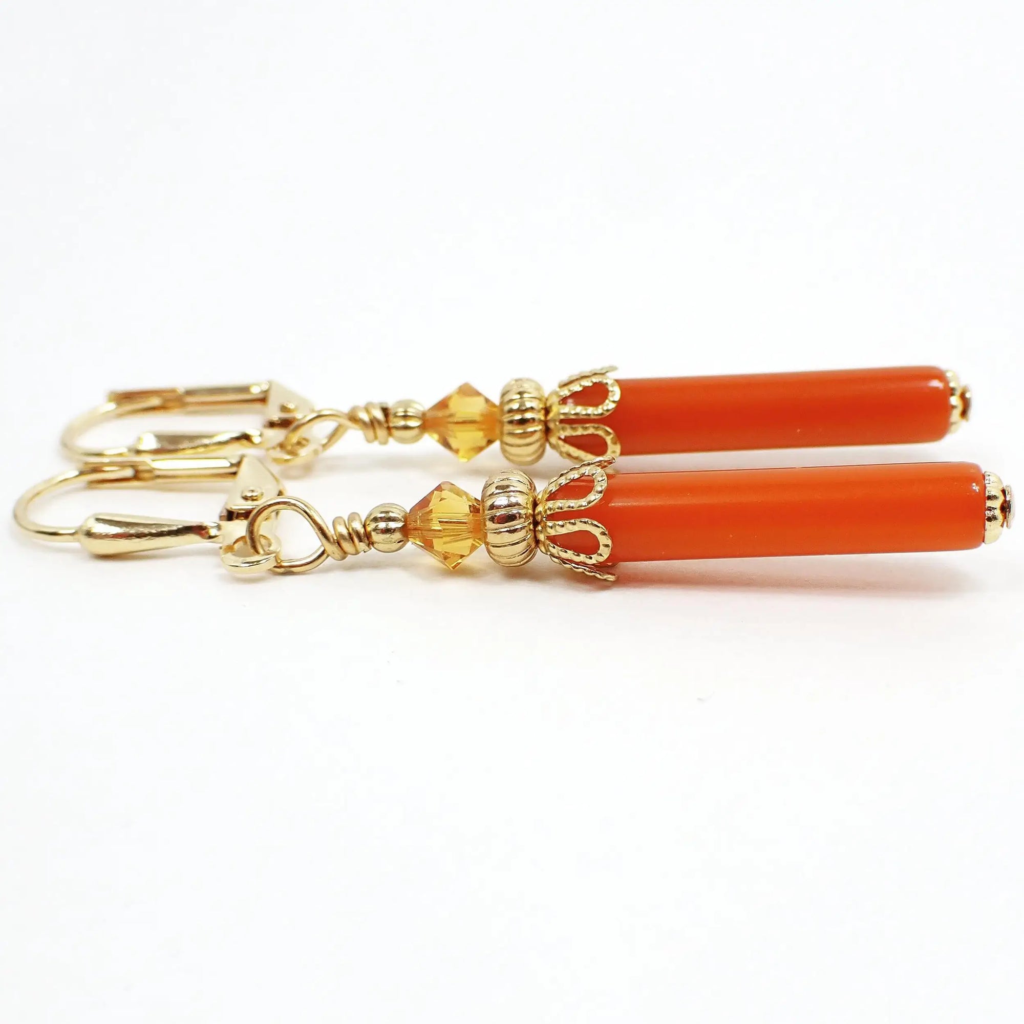 Side view of the handmade stick earrings made with vintage lucite beads. The metal is gold plated in color. There is a light orange faceted glass crystal bead at the top. The bottom beads are thin tube stick beads in a dark orange color lucite.