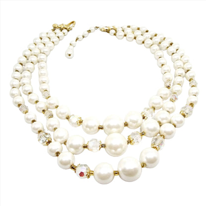 Front view of the Japanese Mid Century vintage multi strand necklace with AB crystal and faux pearl beads. There are three beaded strands with a gold tone color hook clasp at the end. Each strand has white plastic imitation pearl beads and a few AB glass crystal beads towards the bottom of the necklace. There are small gold tone color beads in between the other beads as spacers.