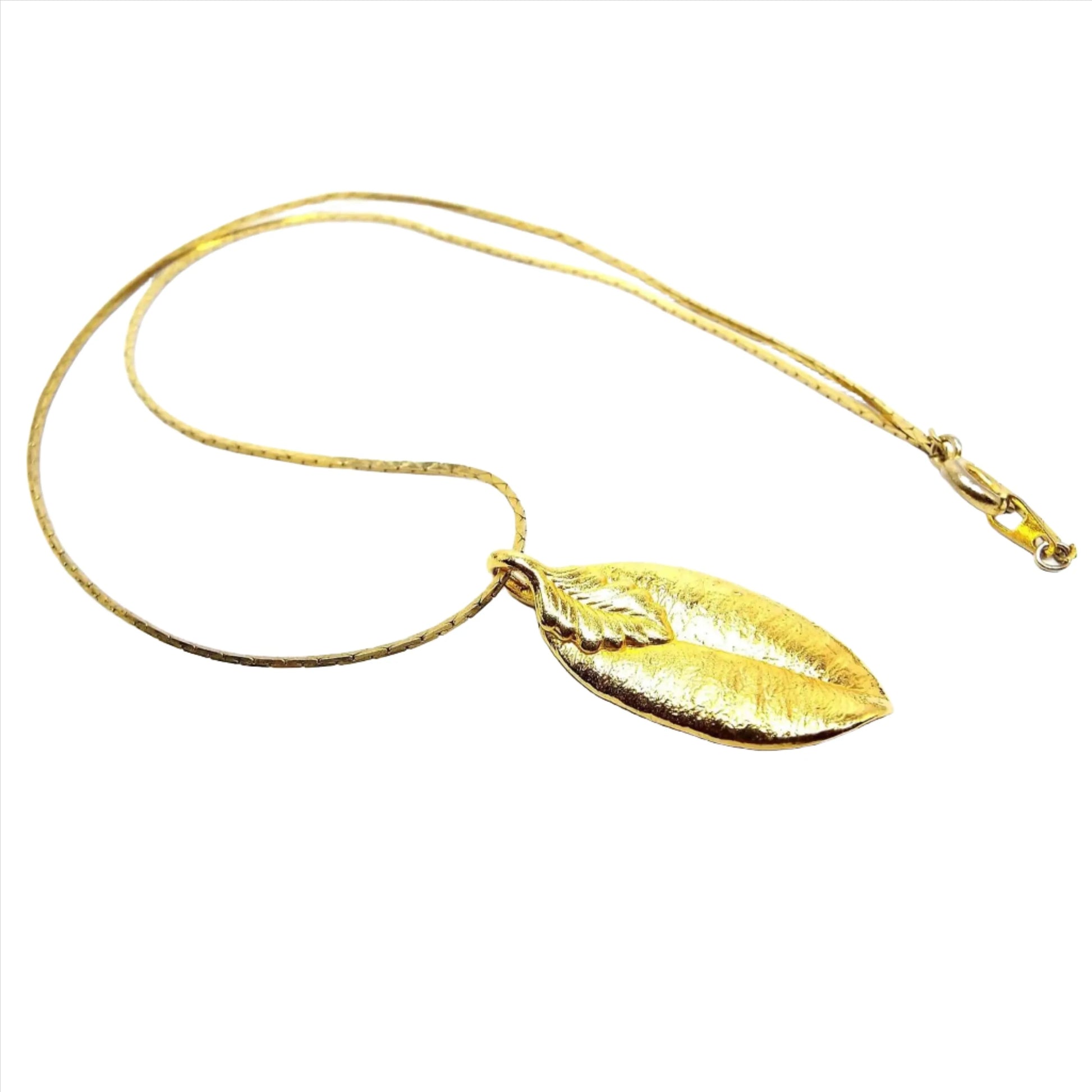 Top view of the retro vintage leaf necklace. It is gold tone in color. It has a thinner style cobra chain with a spring ring clasp at the end. The pendant is a gold plated leaf with gold tone leaf bail.