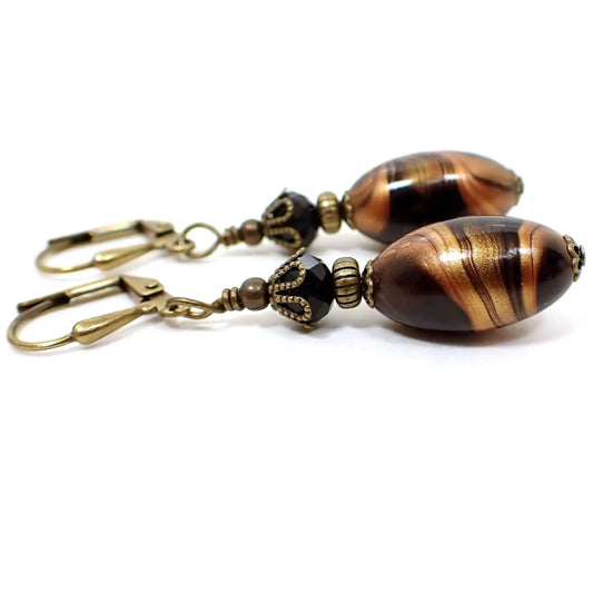 Side view of the handmade lucite earrings. The metal is antiqued brass in color. There are faceted black glass crystal beads at the top. The bottom lucite beads are black and oval in shape with marbled swirls of metallic gold and copper color. 