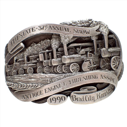 Front view of the retro vintage Siskiyou belt buckle. It's pewter and gray in color. There is a depiction of a steam engine race on the front. The top says Tri State 37th Annual Show and the bottom says Antique Engine and Threshing Assoc 1990 Bird City, KS.