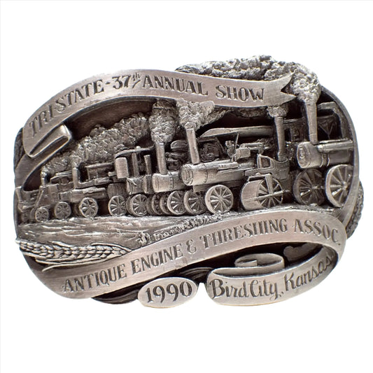 Front view of the retro vintage Siskiyou belt buckle. It's pewter and gray in color. There is a depiction of a steam engine race on the front. The top says Tri State 37th Annual Show and the bottom says Antique Engine and Threshing Assoc 1990 Bird City, KS.