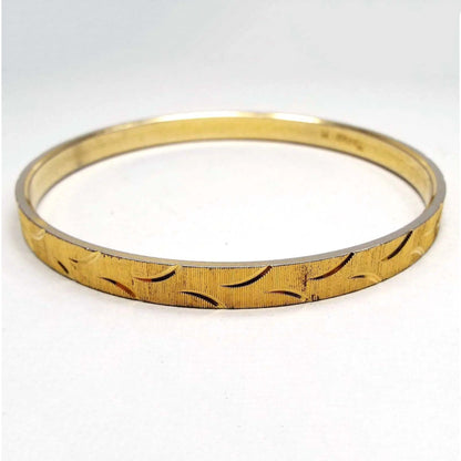 Angled side view of the 1960's Crown Trifari vintage bangle bracelet. It is gold tone in color with an etched pattern of curves and textured lines all the way around the outside edge.