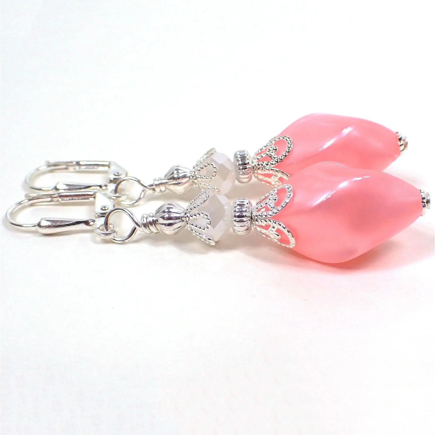 Side view of the handmade drop earrings with vintage lucite beads. The metal is silver plated in color. There are pearly white faceted glass crystal beads at the top. The bottom lucite beads are a twisted oval shape and are pearly pink in color.