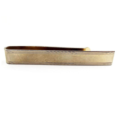 Front view of the Mid Century vintage slide on tie bar. It is a wide long rectangle shape has a light etched design on the edges. The metal is darkened gold tone in color.