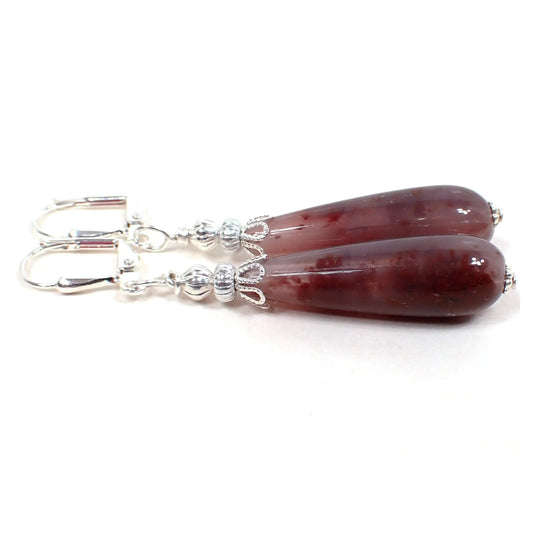 Side view of the handmade teardrop earrings with vintage lucite beads. The metal is silver plated in color. There are two metal beads at the top and a teardrop shaped lucite bead at the bottom. The lucite bead has marbled translucent and opaque shades of plum purple.