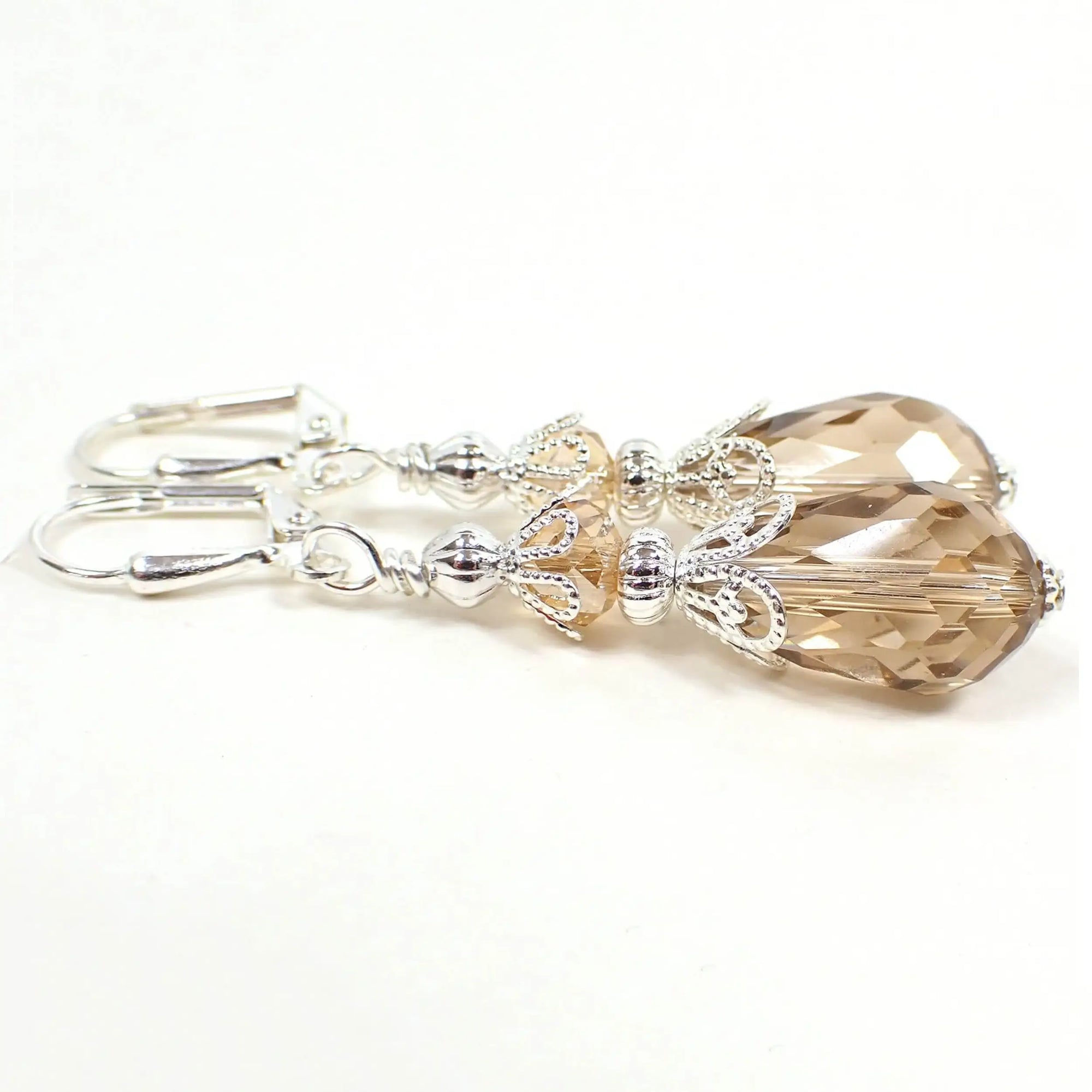 Side view of the handmade teardrop earrings. The metal is silver plated in color. There are faceted glass crystal rondelle beads on the top and teardrop beads on the bottom. The beads are a very light peach champagne color.