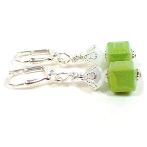 Side view of the handmade small cube earrings. The metal is silver plated in color. There are pearly opaque white glass faceted beads at the top. The bottom square cube beads are lime green in color with a golden sheen around the outside of them.