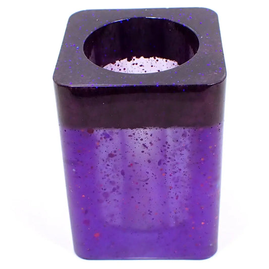 Angled view of the handmade resin makeup brush or toothbrush holder. Nice basic square design with rounded corners. It has dark pearly purple on top with tiny flecks of blue glitter and semi transparent pearly purple resin on the bottom with iridescent chunky glitter here and there. 