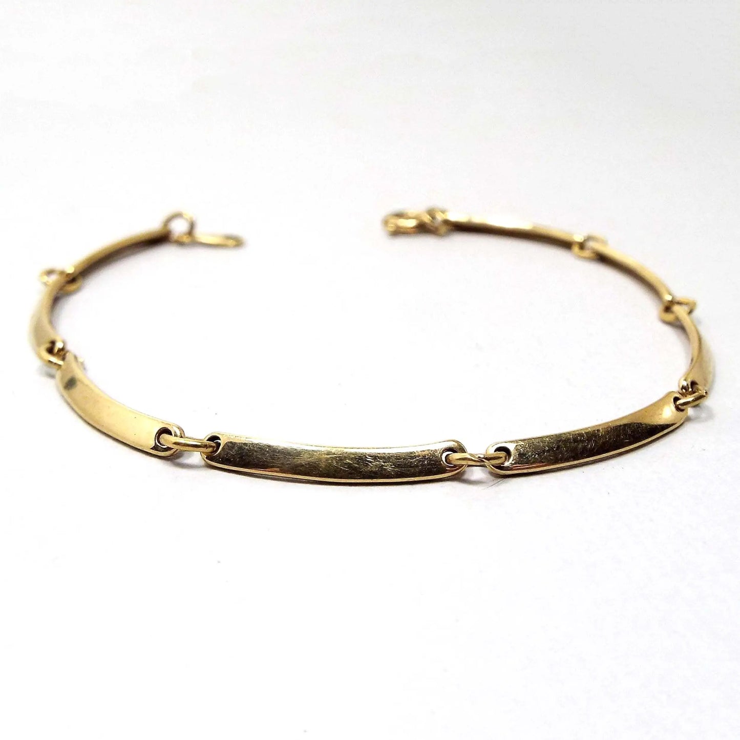 Angled view of the retro vintage Avon link bracelet. The metal is gold tone in color. The links are flattened style long slightly curved oval links held together with metal jump rings. There is a round spring ring clasp at the end.