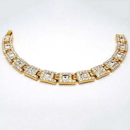 Top view of the 1990's retro vintage rhinestone link bracelet. The metal is gold tone in color. Each link is rectangle shaped with small round pavé set clear rhinestones and one square clear rhinestone on one side of the link. There is a snap lock clasp at the end.