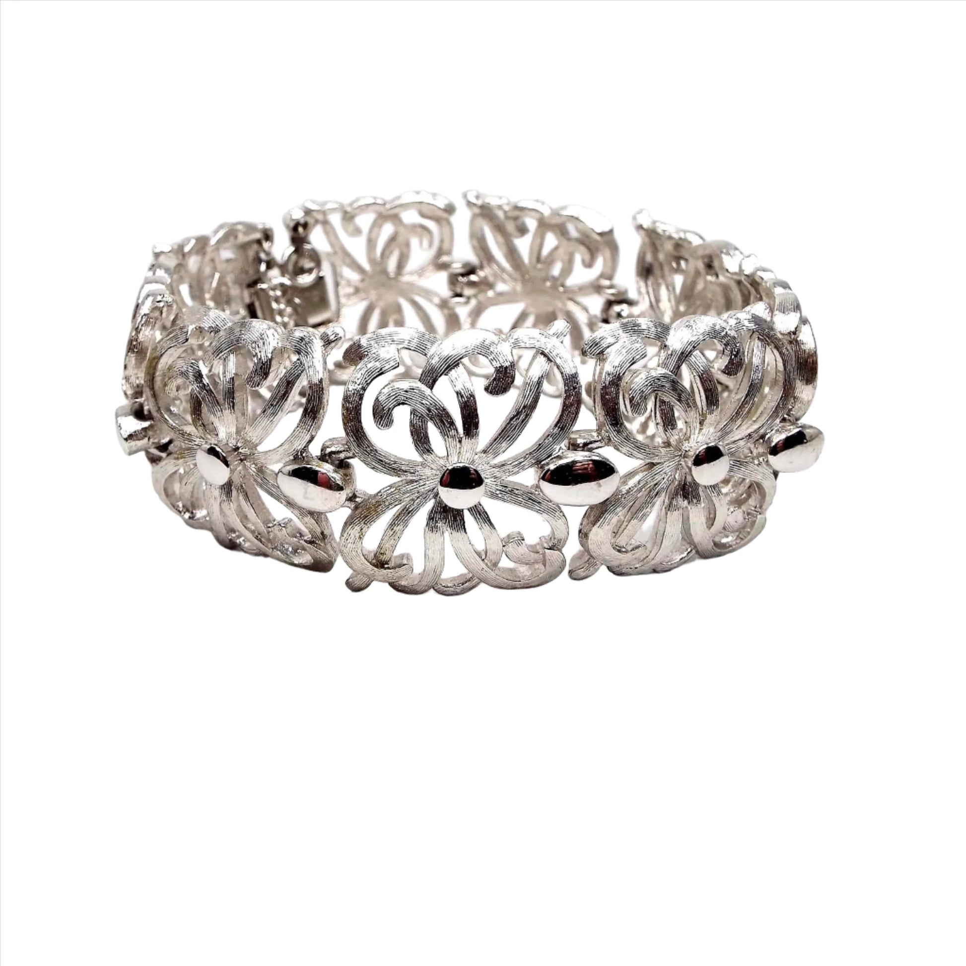 Angled front view of the Mid Century vintage Monet link bracelet. It is silver tone in color and has wide filigree links with a curvy floral like pattern. Most of the bracelet is textured matte metal. There is a snap lock clasp and safety chain on the end.