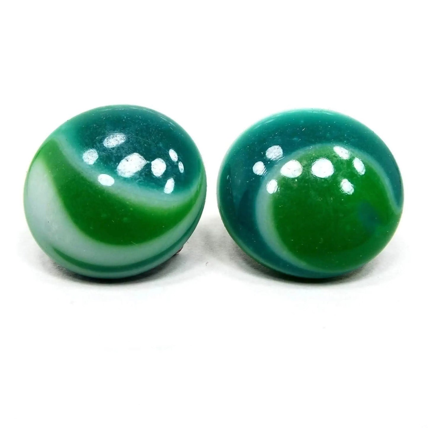 Front view of the Japanese Mid Century vintage clip on earrings. They are domed round in shape. One has curved striped areas of green, teal green, and white and the other has curved round areas of the same colors for an asymmetrical style design.