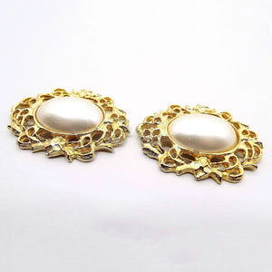 Front view of the retro vintage Bluette vintage shoe clips from the 1980's. The middle areas have large rounded oval pearly white plastic faux pearl cabs. Surrounding the imitation pearl areas is a wreath like filigree design that goes all the way around the edge. The metal is gold tone in color.