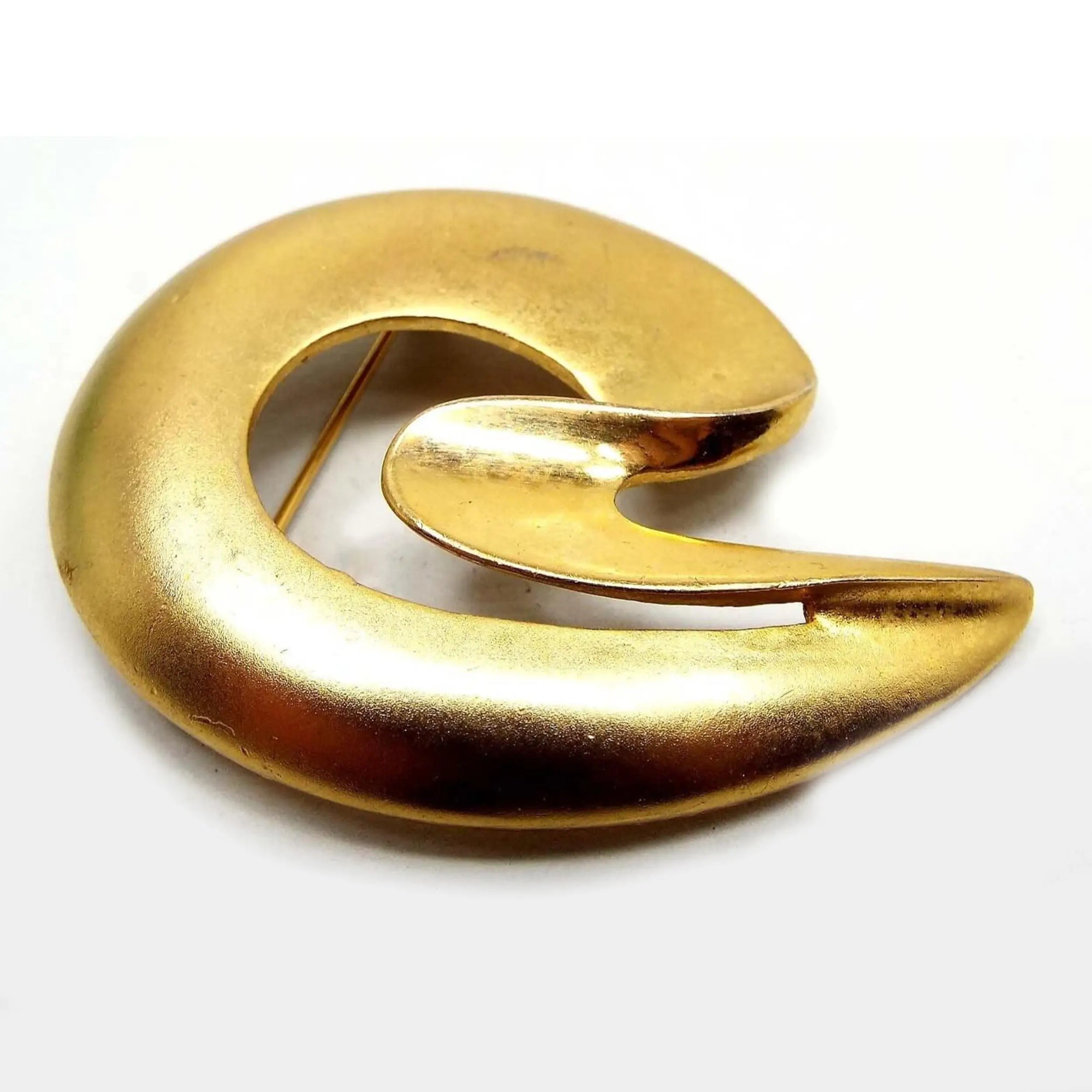 Front view of the retro vintage Mod style brooch pin. It is matte gold tone in color. It has a curved almost C shaped design with an open middle area.