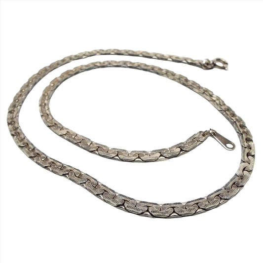 Top view of the retro vintage chain necklace. The silver tone metal is darkened from age to a gray in color. Necklace has a flat style wider C link chain with textured links and a round spring ring clasp on the end.