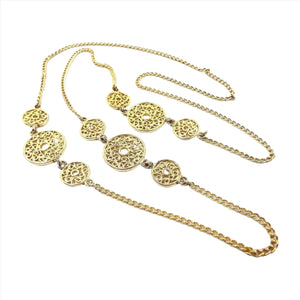 Top view of the long retro vintage chain necklace. The metal is gold tone in color. It has a curb link chain and three areas of fancy links. The fancy links are round with a small open round middle and a filigree curl design throughout the rest of the link. Each set has a large link and two smaller links with the smaller ones on each side of the large. There is no clasp on the necklace as it goes over your head.