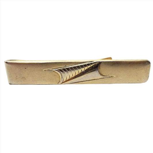 Front view of the 1950's Anson vintage tie bar. Metal is darkened gold in color. It is a long rectangle shape with two modernist style triangles side by side pointing towards each other in the middle. Each triangle has curved indented bottoms. One is plain and the other has curved lines on it. 