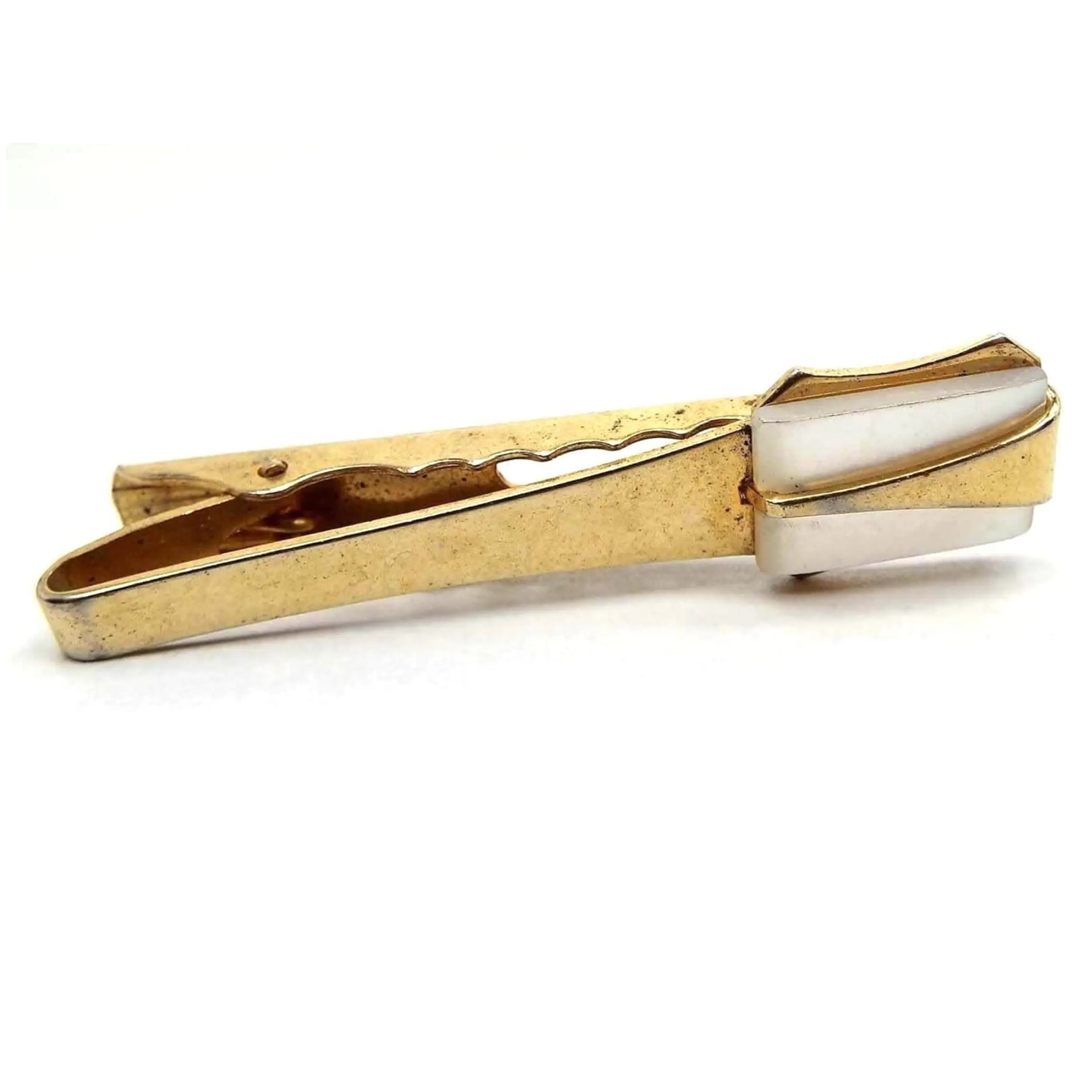 Front view of the Mid Century Anson tie clip. It is gold tone in color with a pearly white rectangle mother of pearl shell cab on the end. There is a gold tone color metal elongated triangle over the mother of pearl cab that has the top point pointing inwards. There is an alligator style clip on the back. There are some tiny dark spots on the metal bar on the front when magnified.