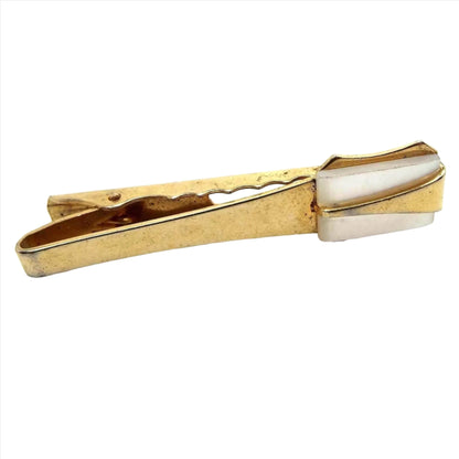 Front view of the Mid Century Anson tie clip. It is gold tone in color with a pearly white rectangle mother of pearl shell cab on the end. There is a gold tone color metal elongated triangle over the mother of pearl cab that has the top point pointing inwards. There is an alligator style clip on the back. There are some tiny dark spots on the metal bar on the front when magnified.