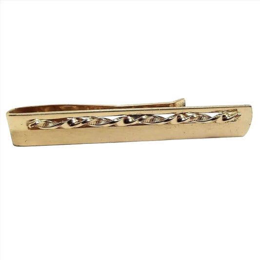 Front view of the Anson Mid Century vintage slide on tie bar. It has a long rectangular shape with a rounded end. The top part has a cut out area with a twisted metal design in it. The back has a curved shorter bar for sliding onto the tie. The tie bar is slightly darkened gold tone in color.