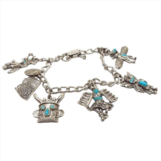 Top view of the 1970's retro vintage Arizona charm bracelet. Bracelet is silver tone in color with a curb link chain and a snap lock clasp on the end. There are 6 charms and a hang tag. The hang tag says Grand Canyon it. The charm shaped like Arizona is sterling silver. The other charms are silver plated Native American Kachina style charms with imitation turquoise cabs.