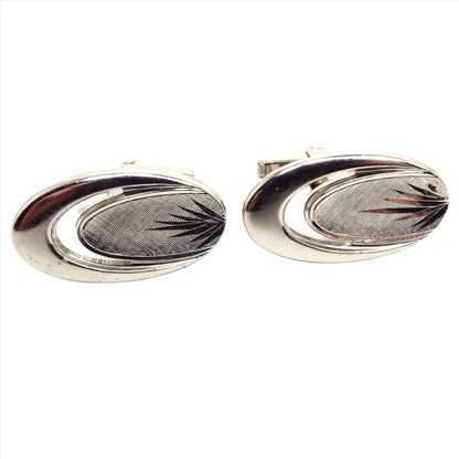 Front view of the retro vintage Foster cufflinks. The metal is silver tone plated in color. They are oval in shape with an open stretched C shape area on the left. The right hand side has textured metal and an etched cut partial starburst shape for an Atomic like design.