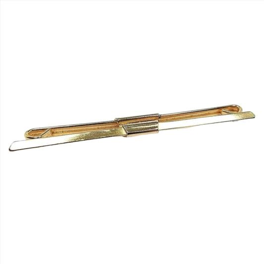 Angled front and side view of the Mid Century vintage collar clip bar. The metal is gold tone in color. The front of the bar is straight and has a tapered angled front edge. The back bar is straight and curls inwards at the ends. There is a rectangular piece in the middle that secures the bars together.