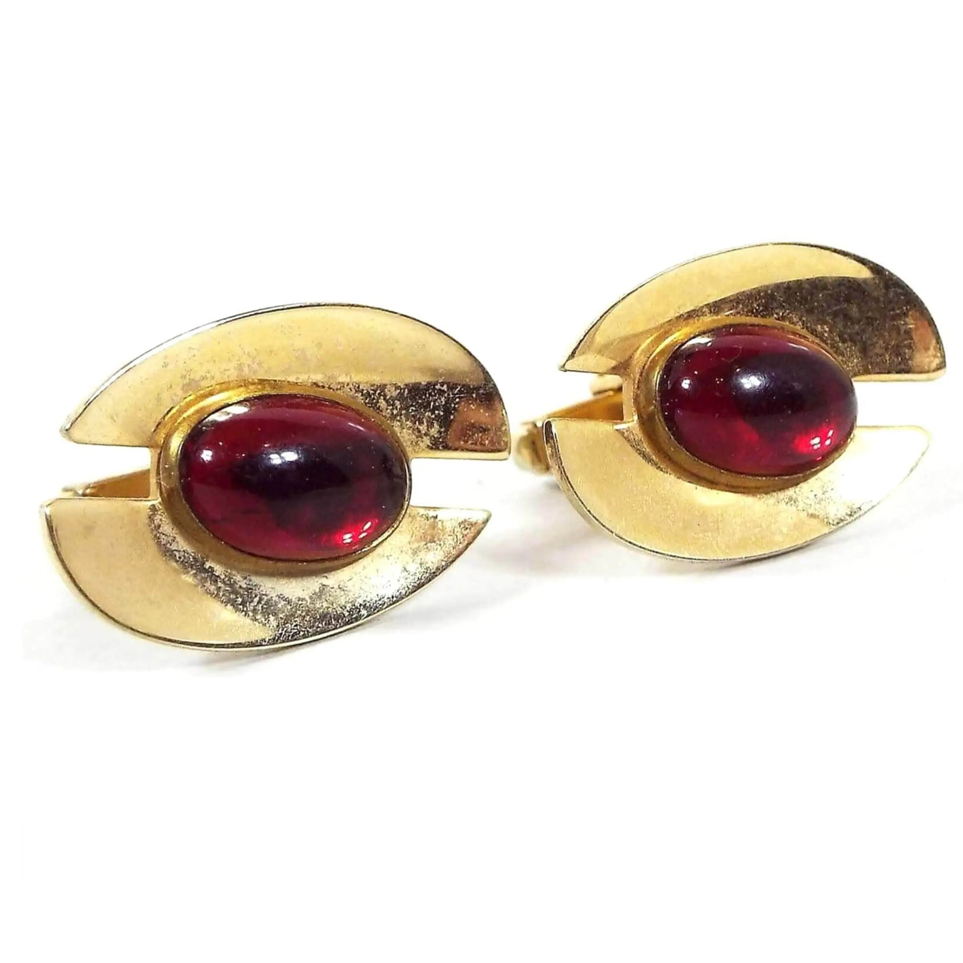 Front view of the Mid Century Anson vintage cufflinks. They are gold tone metal in color with a Modernist style split oval shape. In the middle are puffed oval lucite plastic cabs in a deep red color. There is some light spotting on the plating when seen under magnification.