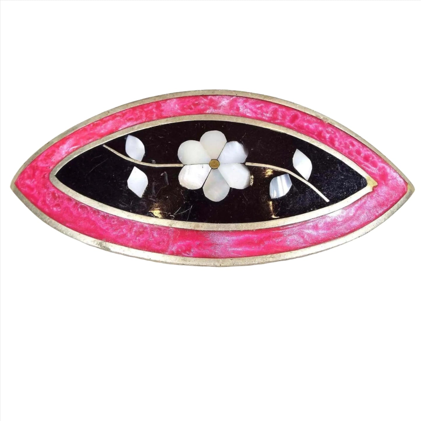 Front view of the retro vintage mexican hair clip. It is a large marquis shaped piece with silver tone color metal. The inside area has black enamel with pearly white pieces of inlaid mother of pearl shell to form a floral design with a set of leaves on each side of the flower. The other edge has pink pearly enamel.