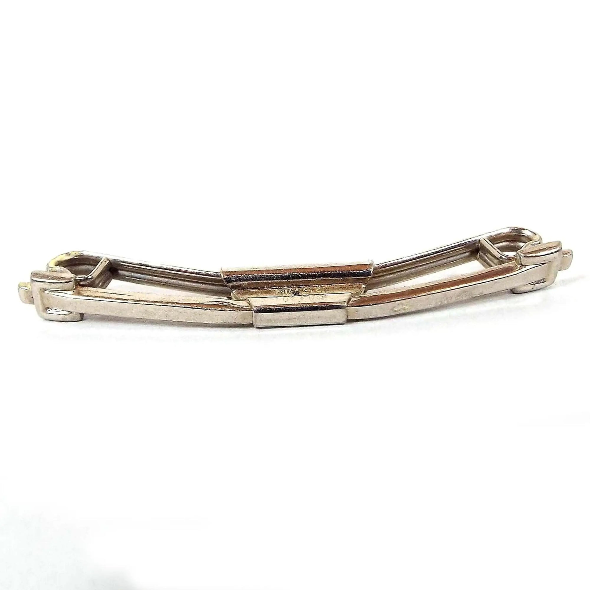 Front view of the 1920's Art Deco vintage Swank collar clip bar. The metal is silver tone in color. The front bar is curved and thin with a squared belt buckle style design on the metal at the ends. The back is curled inwards at the ends. There is a rectangular area in the middle holding the bars together. Part of the stamped patent number can be seen on the side of the middle area.
